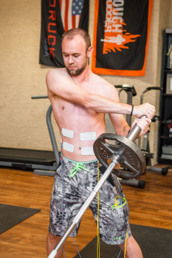 remote Athlete performing landmine rotation exercise with electrical stimulation pads on core to improve strength and movment efficiency using Phoenix Waveform